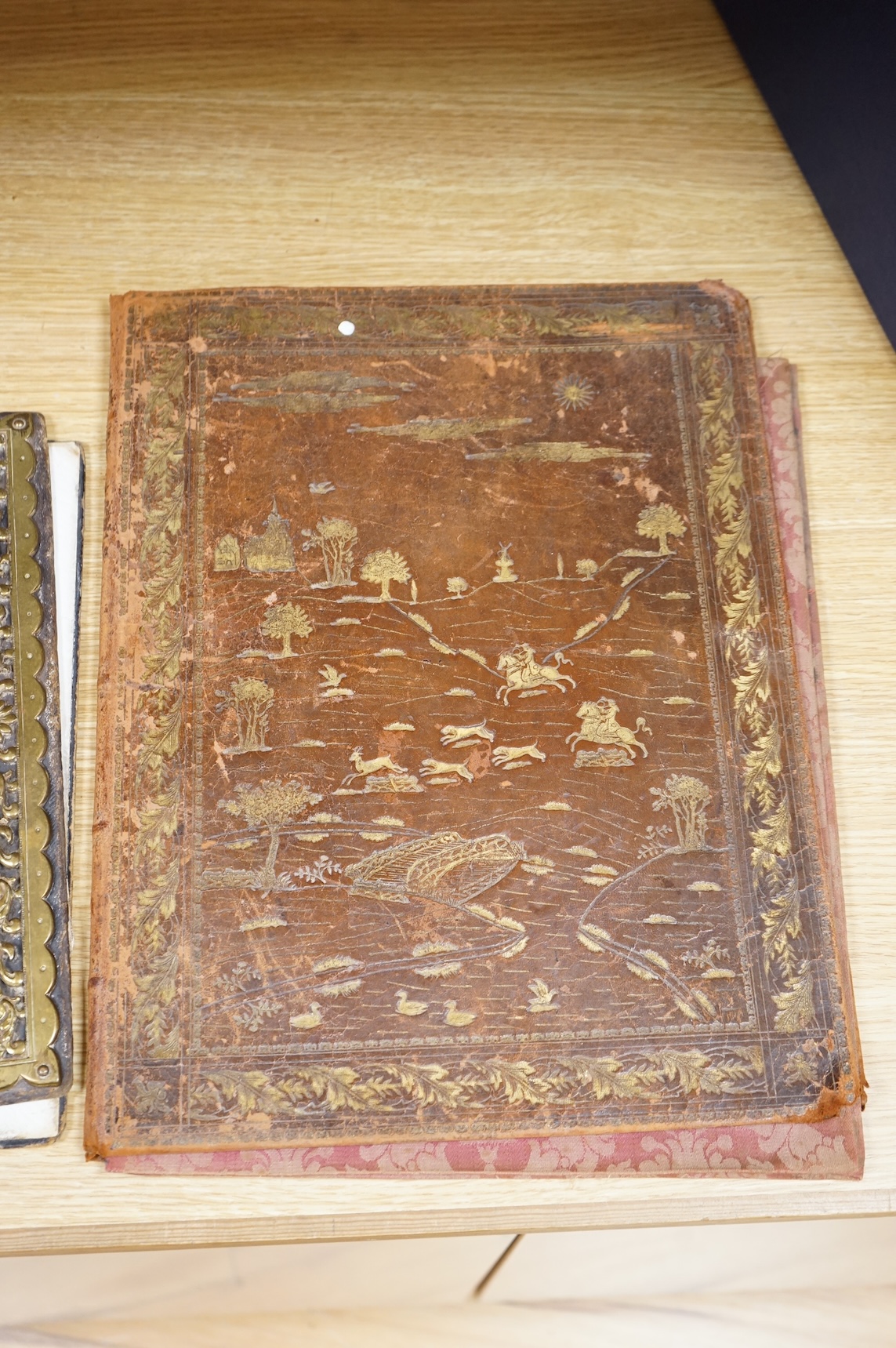 An ornate brass mounted and Morocco leather blotter and a tooled leather blotter of a Persian hunting scene with a red damask lining